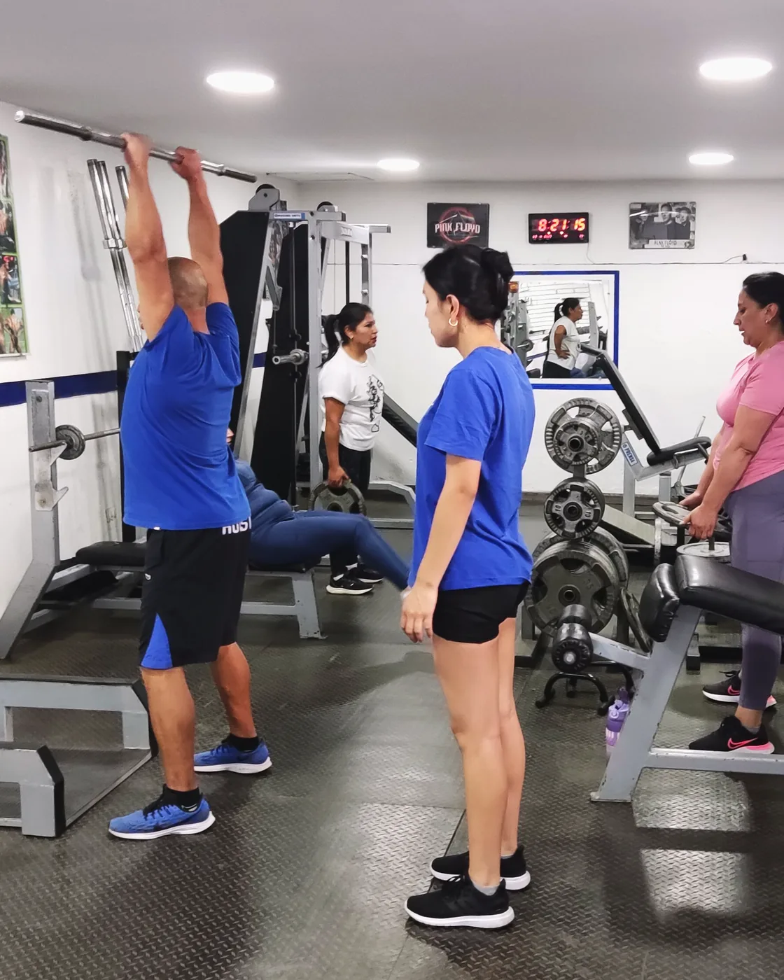 Zona de pesas del Gimnasio RC con barras, discos y bancos, y un socio entrenando con supervisión.